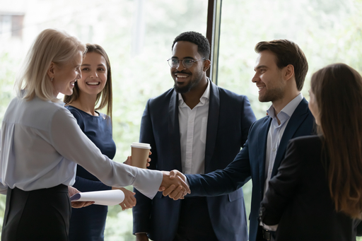 Older woman introducing and shaking hands with a group of four young diverse professionals